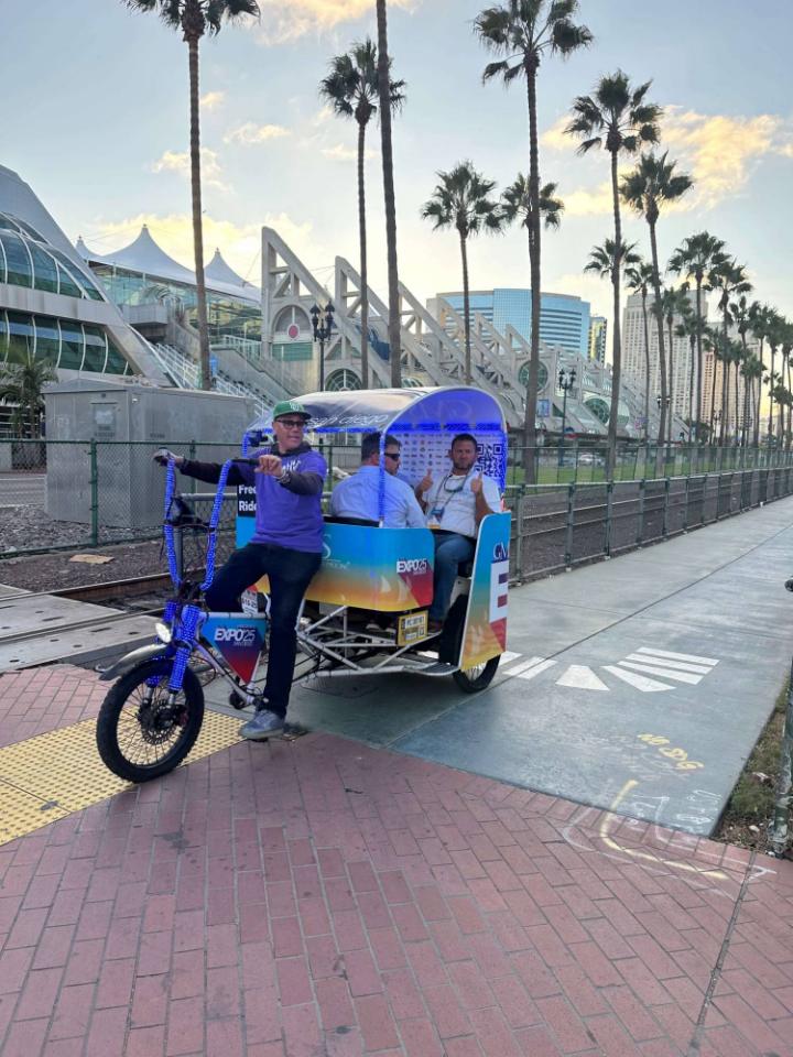 Riders in an expo-wrapped pedicab outside the San Diego Convention Center at sunset