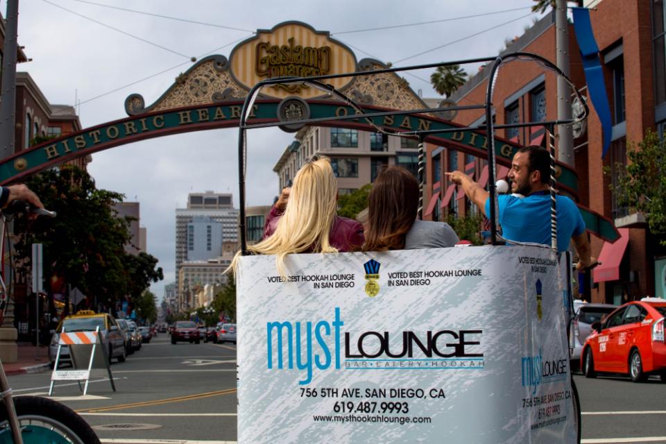 Two riders and their driver heading under the Gaslamp Quarter arch in a pedicab wrapped for a local lounge