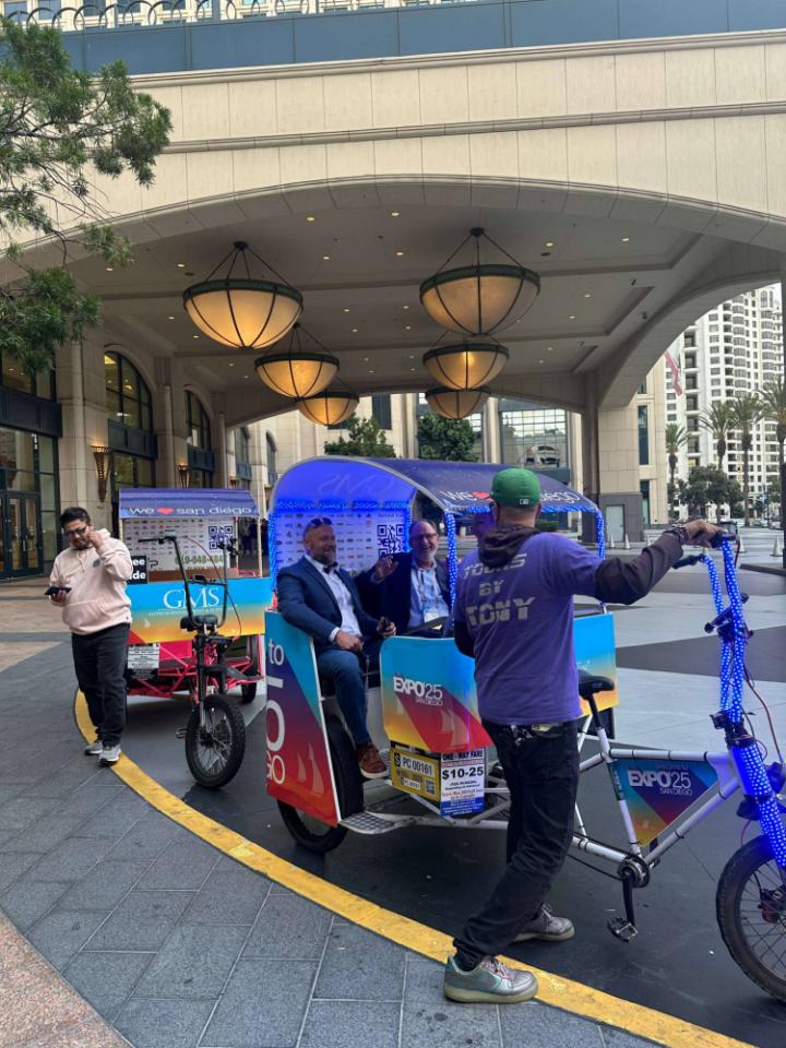 Expo attendees laughing in an LED-lit, expo-wrapped pedicab at a downtown hotel entrance