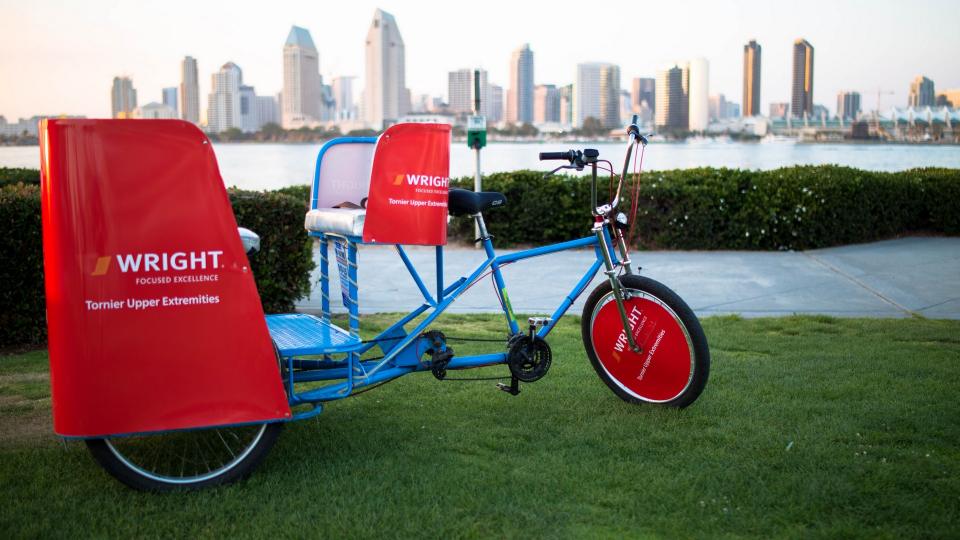 A sponsor-wrapped pedicab on the lawn with the downtown San Diego skyline across the bay